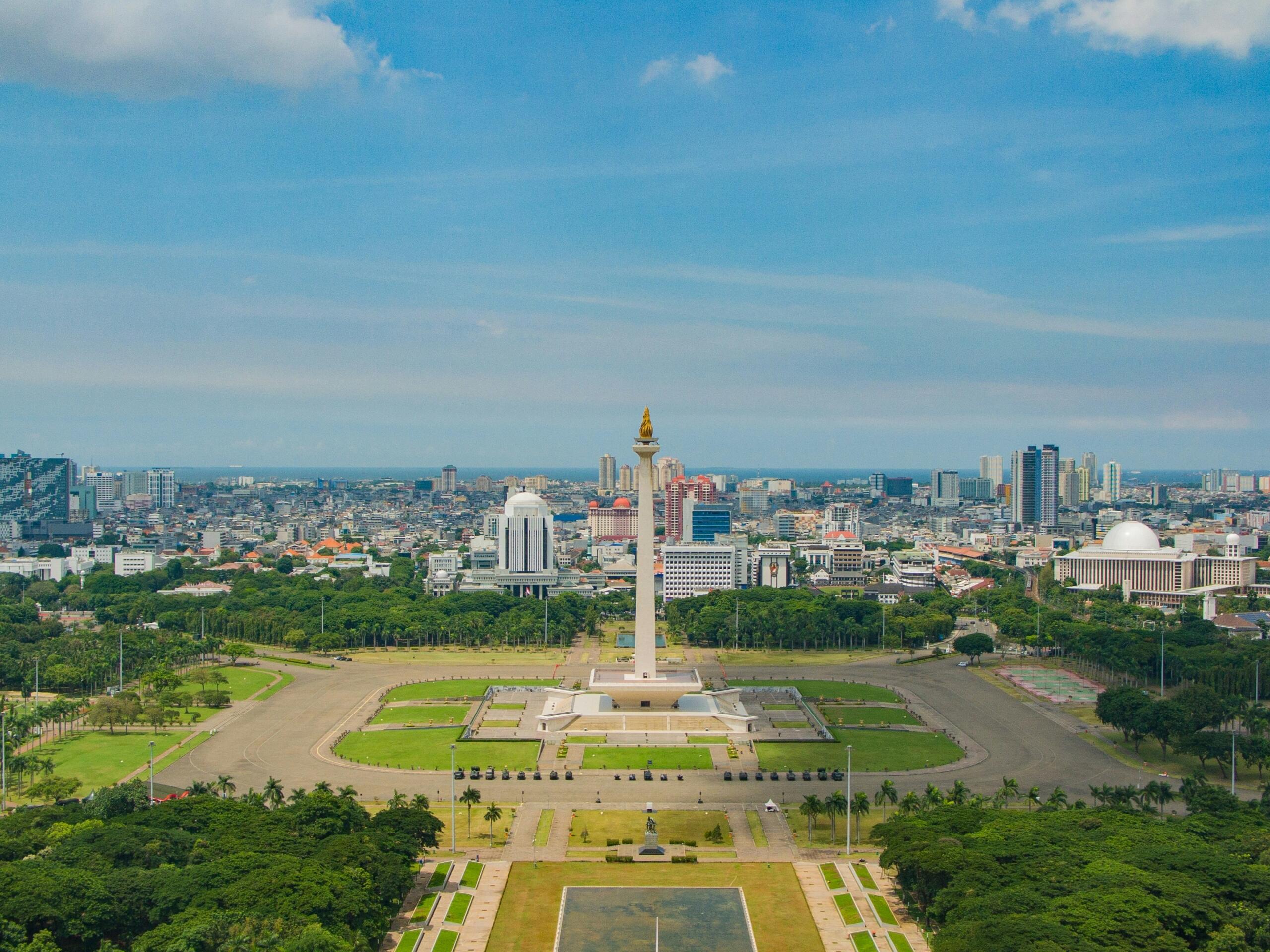 Jakarta cityscape featuring the National Monument prominently in the foreground with the skyline in the background.
