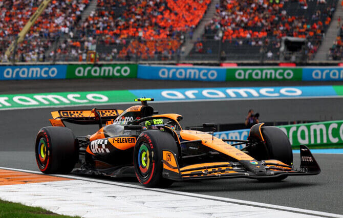 A racing car with an orange and black paint job speeds around a track, showcasing its dynamic design and performance.